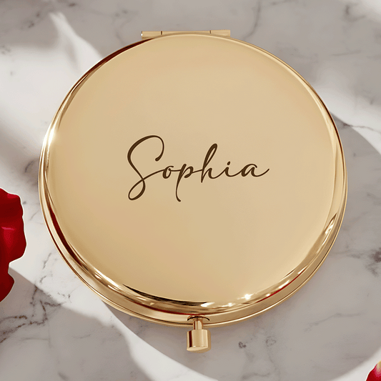 Gold round compact mirror with a custom name engraved in elegant script beside red rose petals