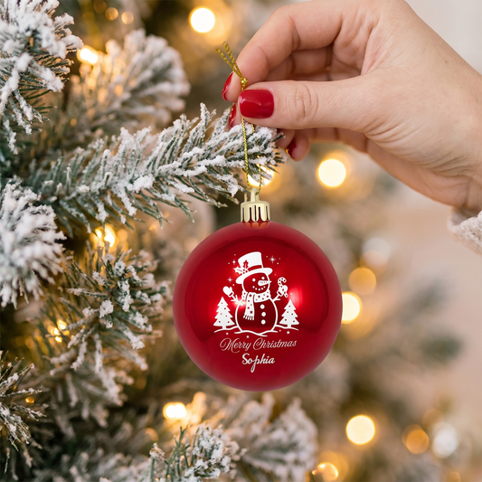 Hand with red nails hanging a red snowman Merry Christmas name ornament on a frosted tree
