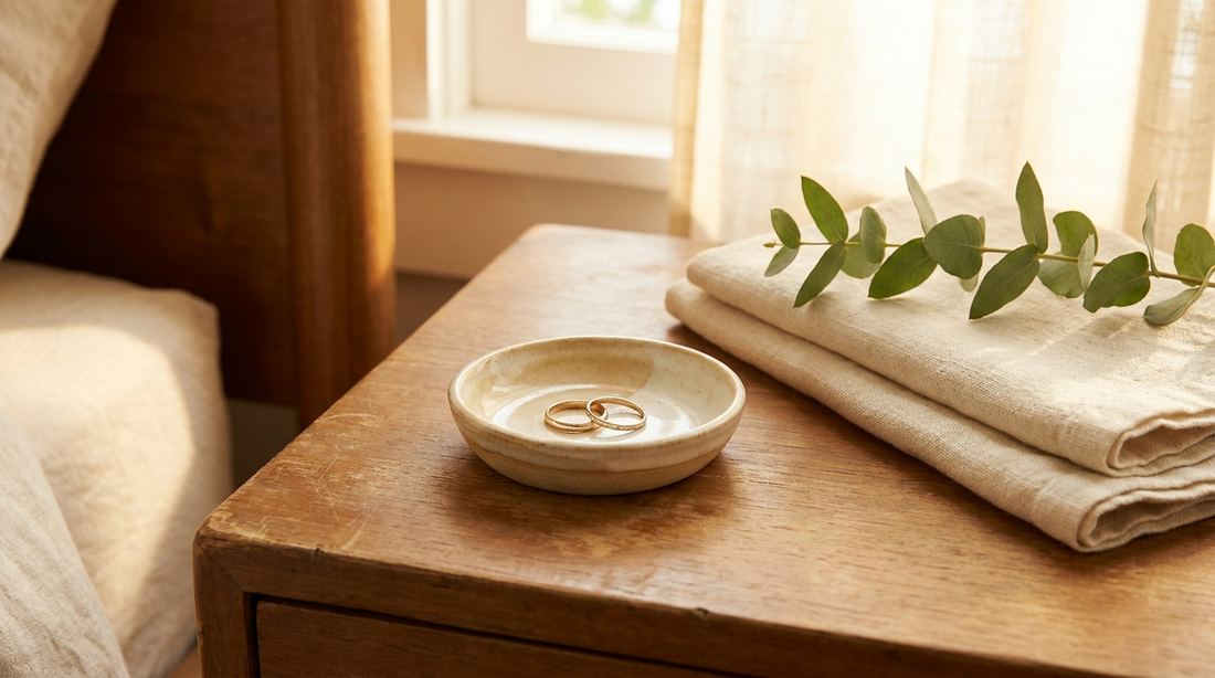 Small ceramic ring dish holding two rings on a bedside table beside folded linen