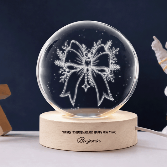 Crystal ball engraved with an elegant ribbon bow and festive foliage on a wooden base reading Merry Christmas and Happy New Year