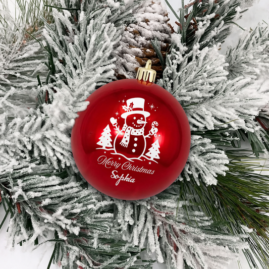 Red ball ornament with white line art snowman, trees and Merry Christmas custom name on flocked pine