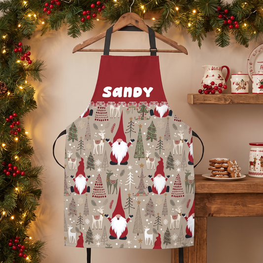 Red and beige Christmas gnome print apron with white custom name on a hanger under garland
