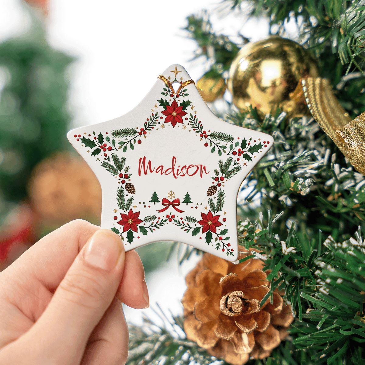 Hand holding the poinsettia wreath ceramic star ornament near a pinecone
