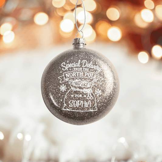 Silver glitter Special Delivery From The North Pole bauble with custom name on a bokeh background