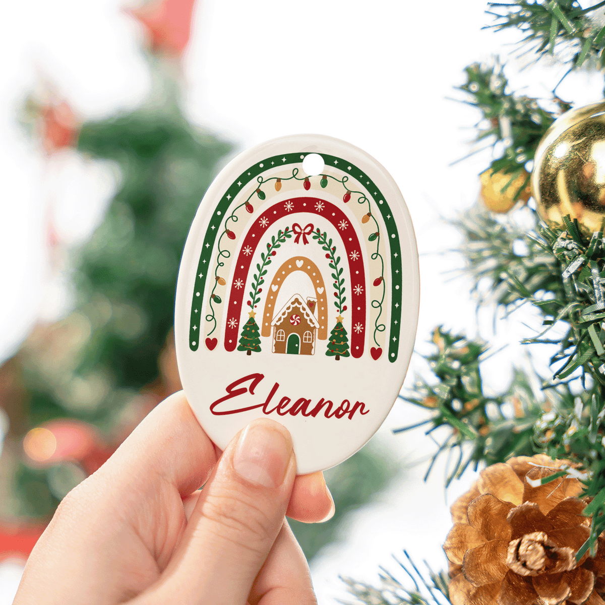Hand holding the oval Christmas rainbow ceramic ornament with custom name