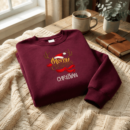 Maroon Merry Christmas reindeer custom name sweatshirt folded on a knit blanket