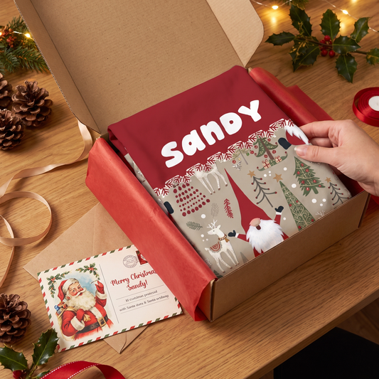 Hand unboxing a red gnome pattern custom name apron from a kraft box with a Santa postcard