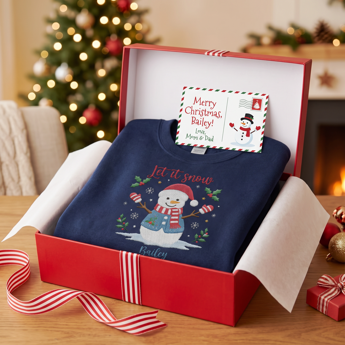 Navy Let It Snow snowman name sweatshirt in a red gift box with a Merry Christmas postcard