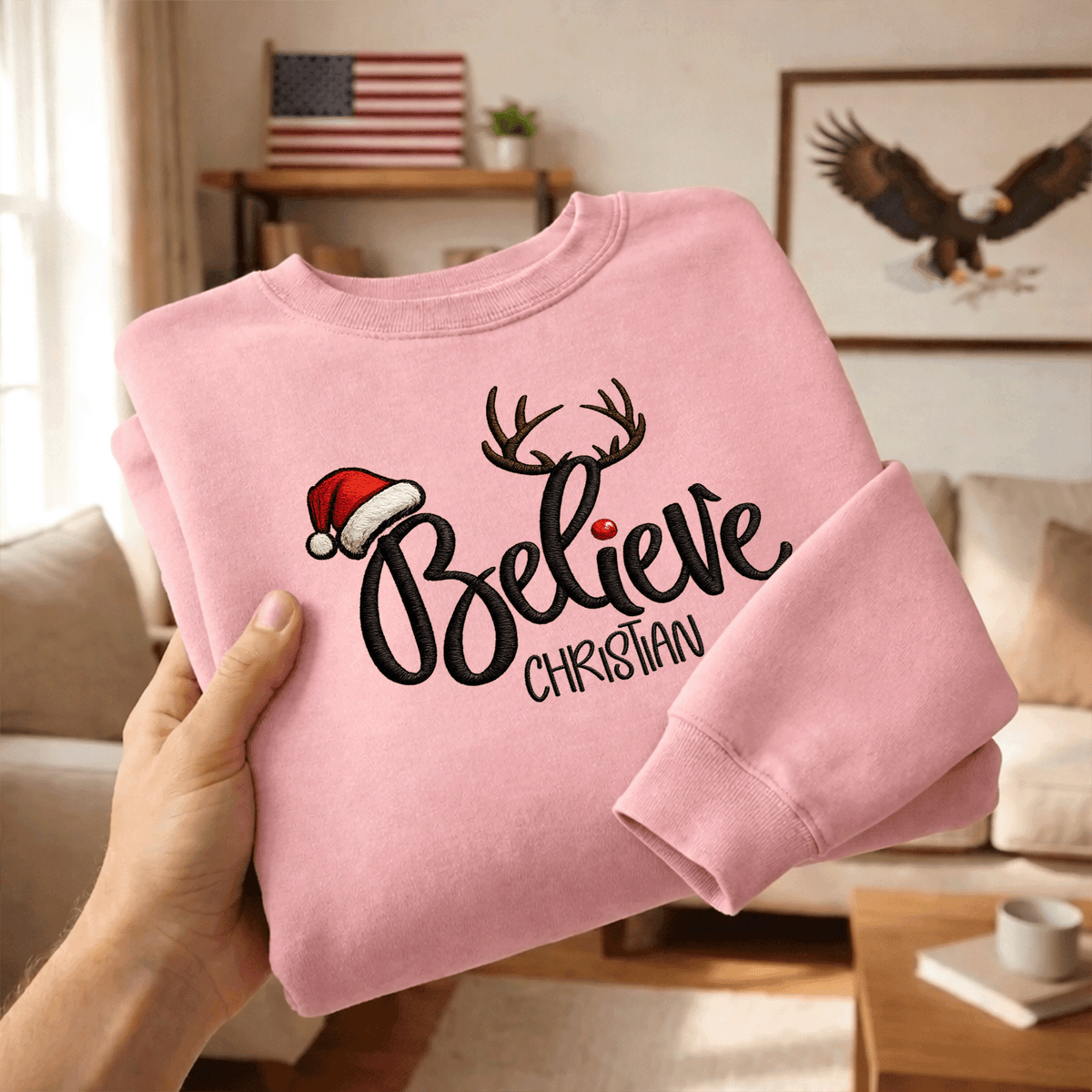 Hands holding a folded pink Believe antlers embroidered sweatshirt