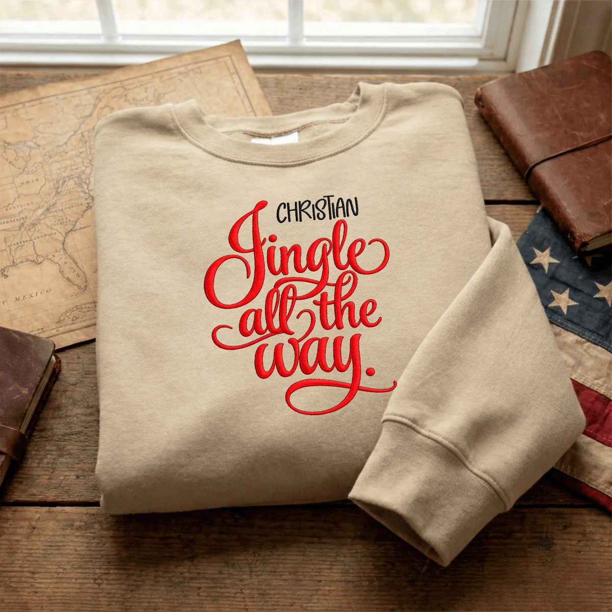 Sand Jingle All the Way name sweatshirt folded on a map