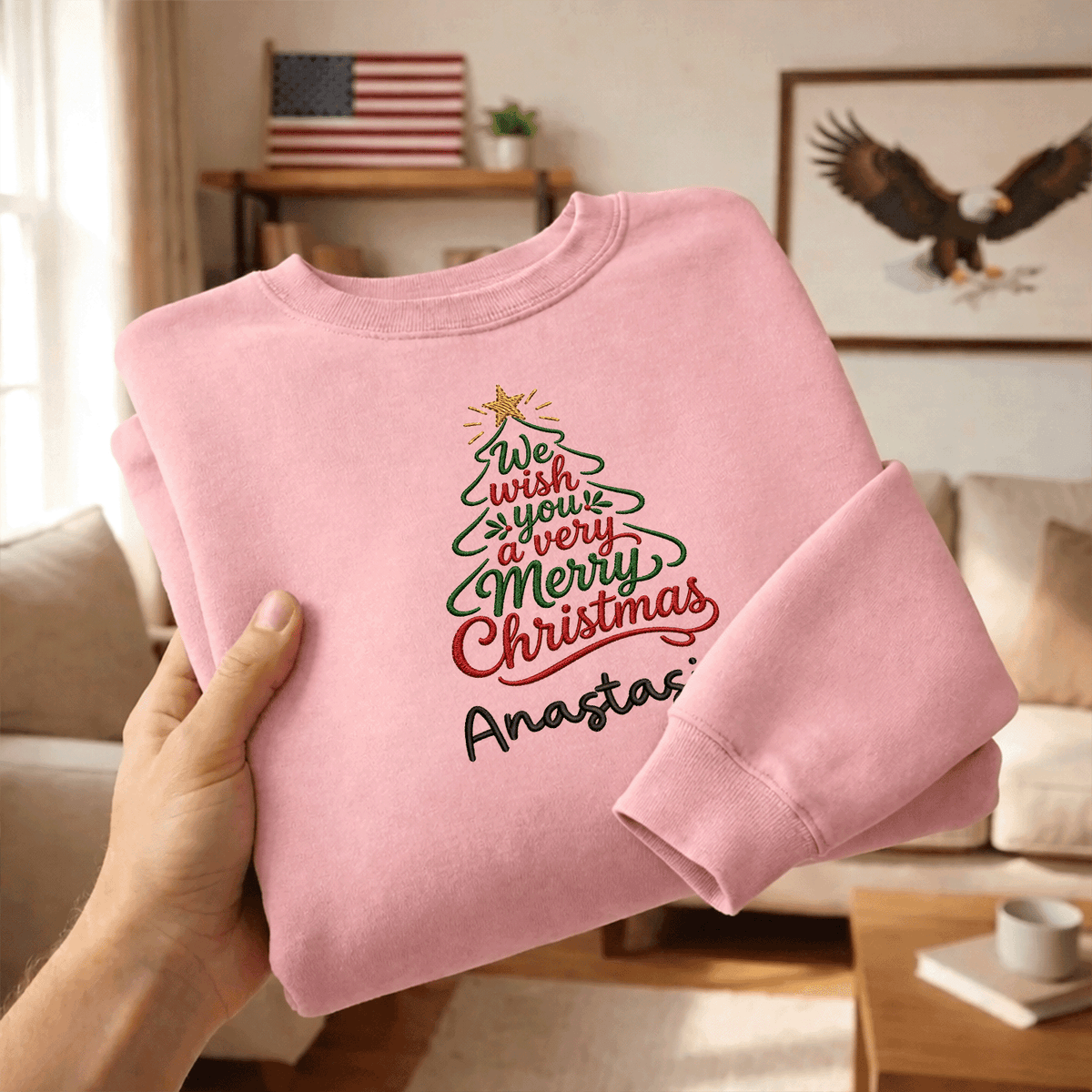 Hands holding a folded pink We Wish You a Merry Christmas sweatshirt