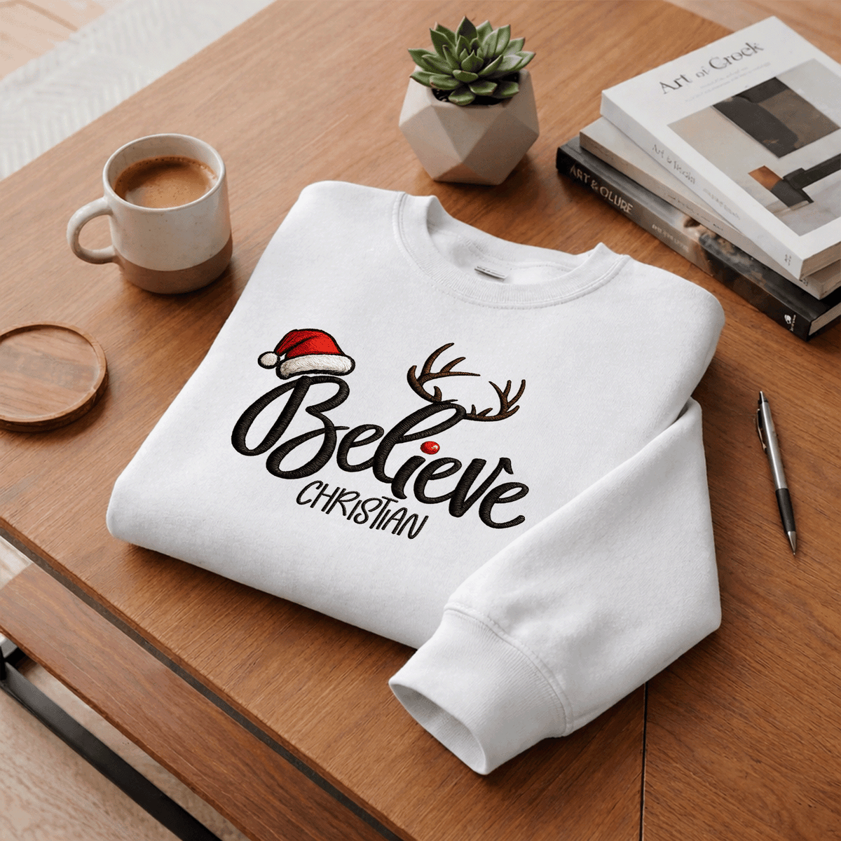 White Believe antlers custom name sweatshirt folded on a desk with coffee
