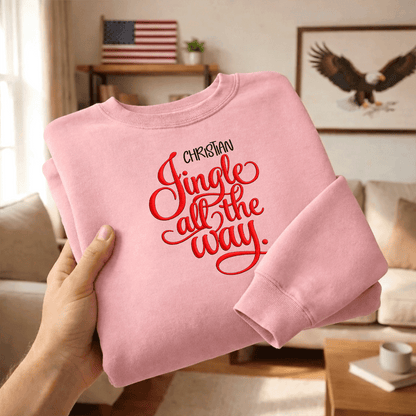 Hands holding a folded pink Jingle All the Way embroidered sweatshirt