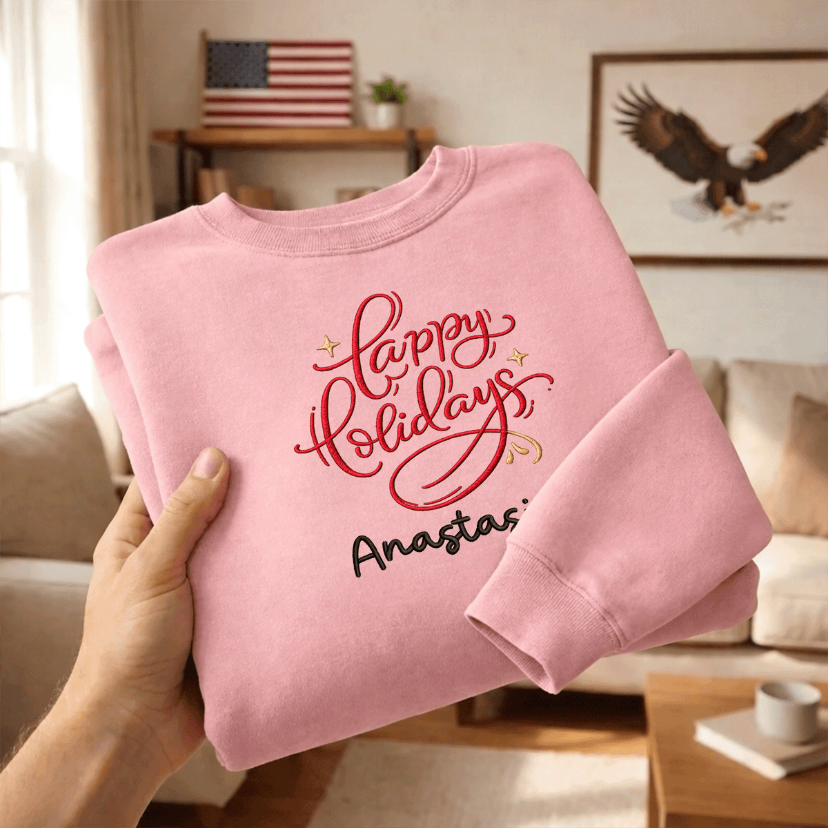 Hands holding a folded pink red Happy Holidays embroidered sweatshirt