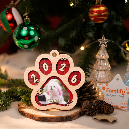 Custom paw print dog photo ornament standing on a wood slice beside Christmas baubles and pinecones
