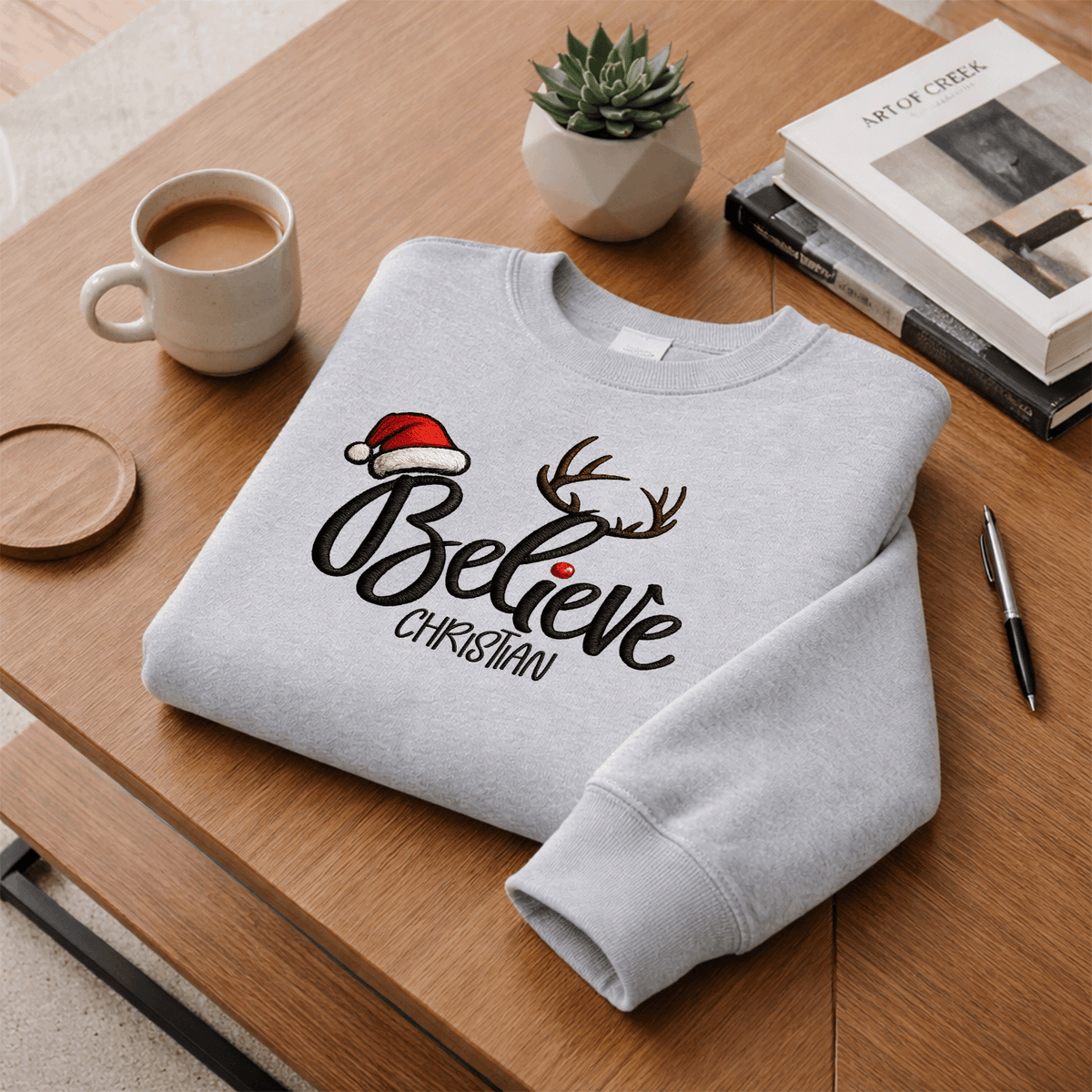 Heather grey Believe reindeer antlers sweatshirt folded on a desk