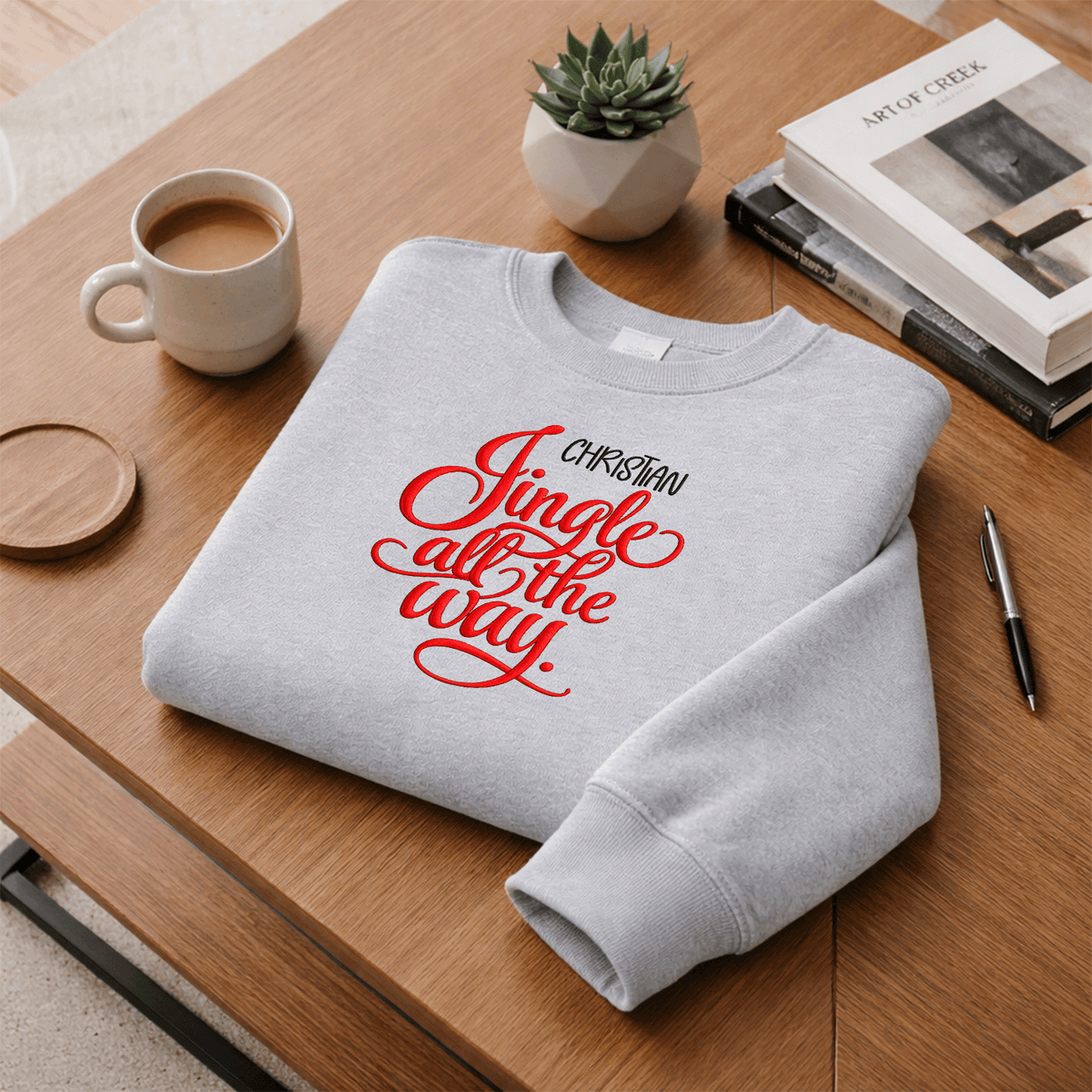 Heather grey Jingle All the Way sweatshirt folded on a desk