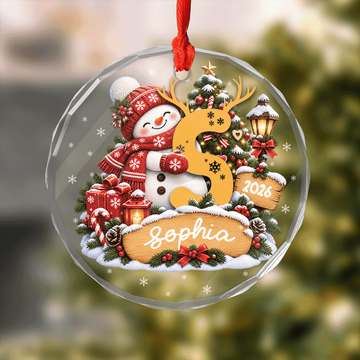 Round clear glass ornament printed with a snowman hugging an antlered initial letter, custom name and year