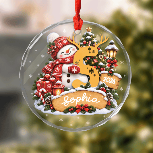Round clear glass ornament printed with a snowman hugging an antlered initial letter, custom name and year