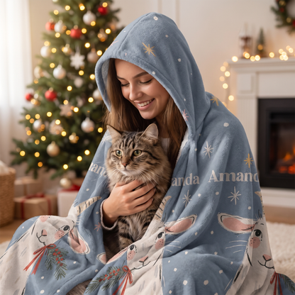 Smiling woman snuggled in the Christmas Goats Starry Night hooded blanket with her cat by the Christmas tree