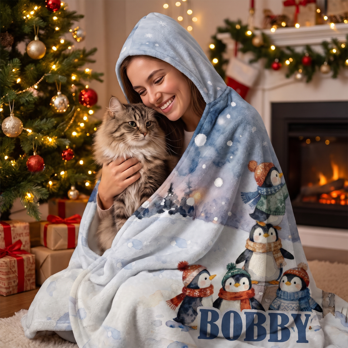 Smiling woman snuggled in the Penguins Snowy Mailbox hooded blanket with her cat by the Christmas tree