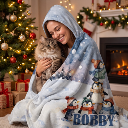 Smiling woman snuggled in the Penguins Snowy Mailbox hooded blanket with her cat by the Christmas tree