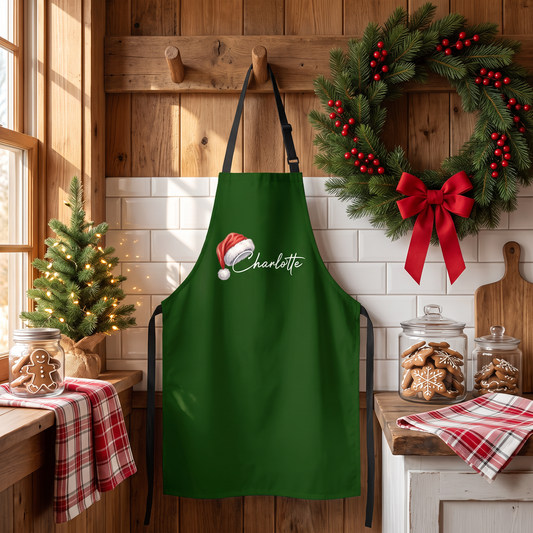 Green Santa hat custom name apron hanging on a wooden hook by a wreath and cookie jars