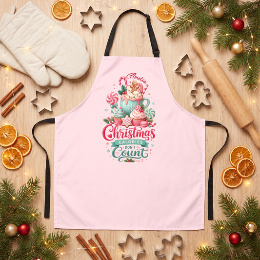 Pink apron with a candy and cocoa mug design reading Christmas Calories Don't Count and custom name, flat lay