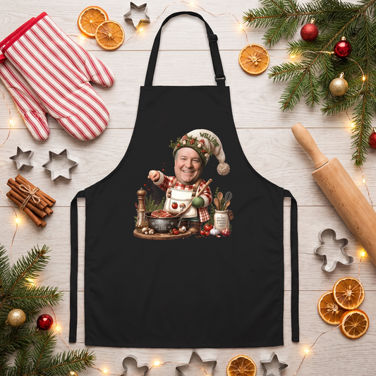 Black apron with a custom photo face elf chef in a stocking cap stirring a pot and custom name, flat lay