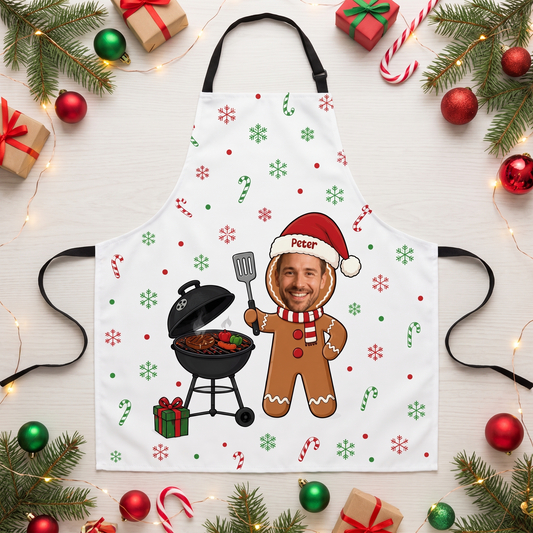 White snowflake apron with custom photo face gingerbread man beside a grill and custom name, flat lay