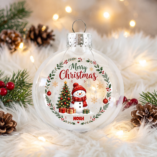 Clear snowman Merry Christmas name ornament resting on white fur with pinecones and fairy lights