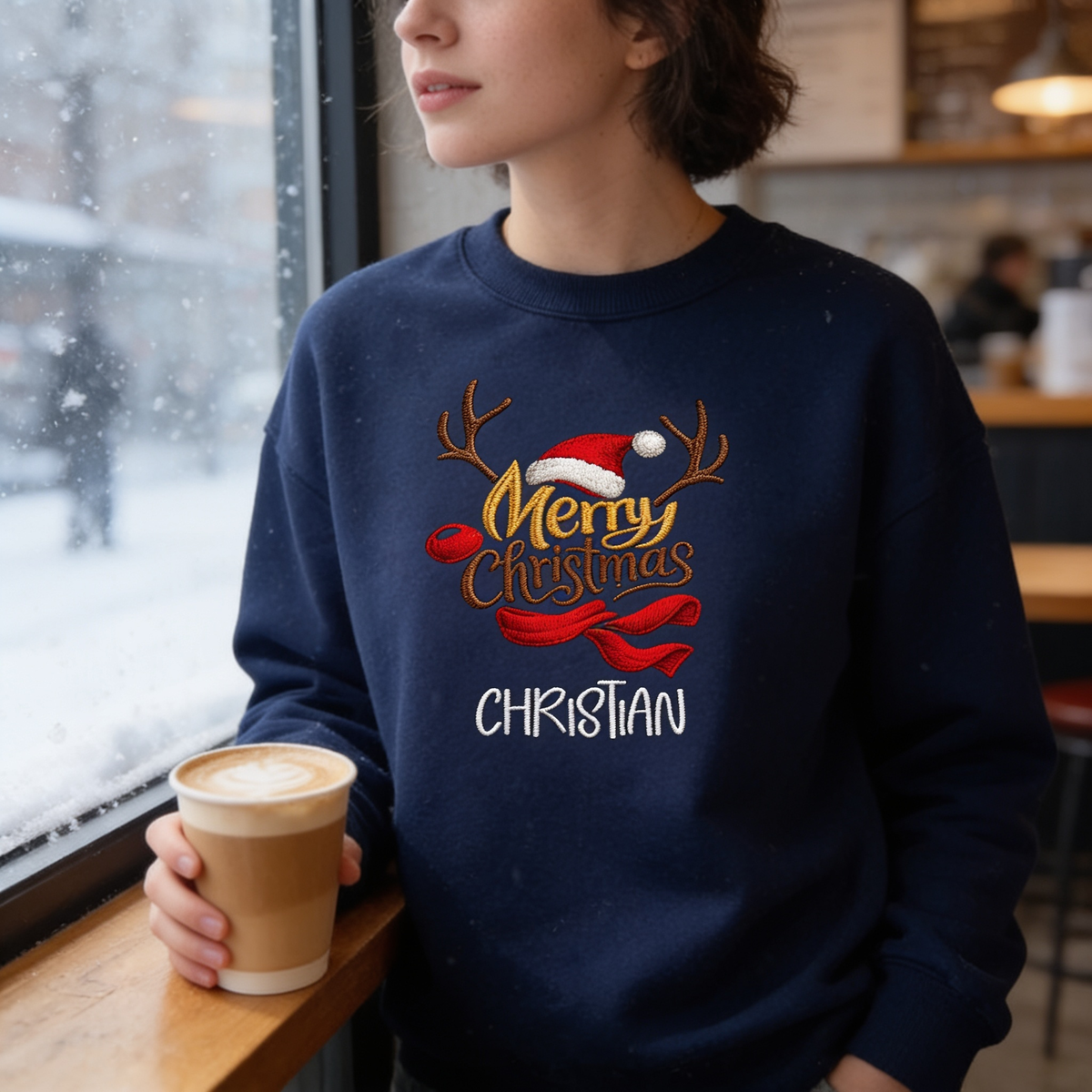 Woman in a navy sweatshirt embroidered with gold Merry Christmas, reindeer antlers, Santa hat, red scarf and custom name