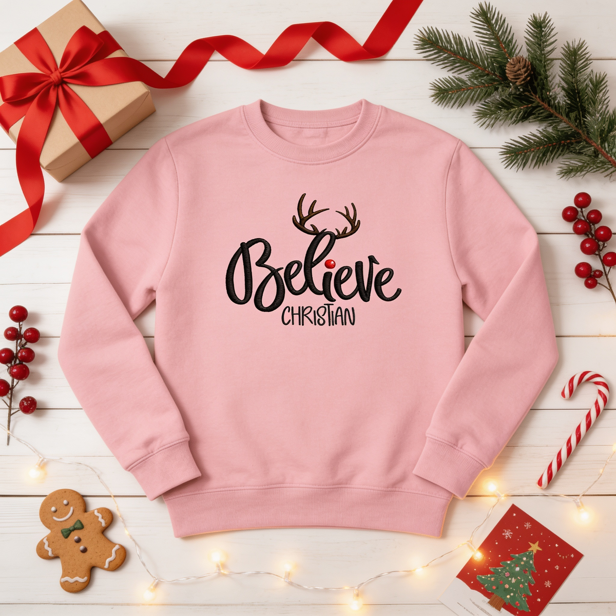 Pink sweatshirt embroidered with Believe in black script with reindeer antlers and a custom name