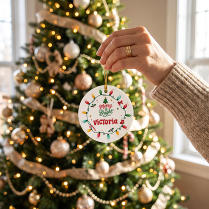 Hand hanging the Merry and Bright ceramic ornament on a gold and white tree