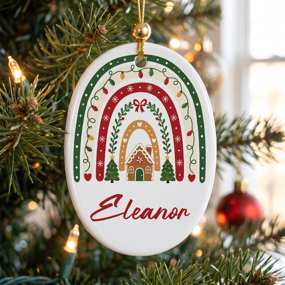 Oval white ceramic ornament with a Christmas rainbow, gingerbread house and custom name in red script