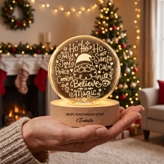 Hand holding a glowing crystal ball engraved with a Santa face and words Ho Ho Ho, Joy, Peace, Believe in Magic