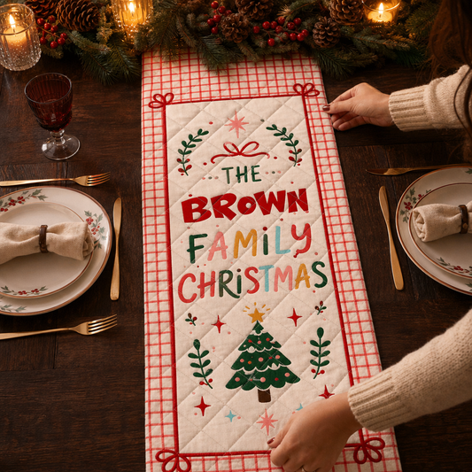 Hands placing a red grid quilt runner with colorful The custom family name Christmas lettering, bows and a small tree