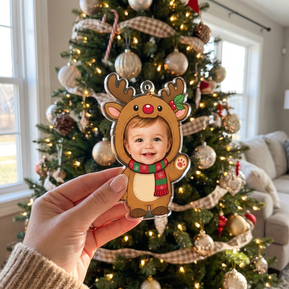 Hand holding the personalized baby reindeer suit ornament in front of a Christmas tree