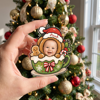 Hand holding the personalized gingerbread bear cocoa mug baby ornament by a Christmas tree