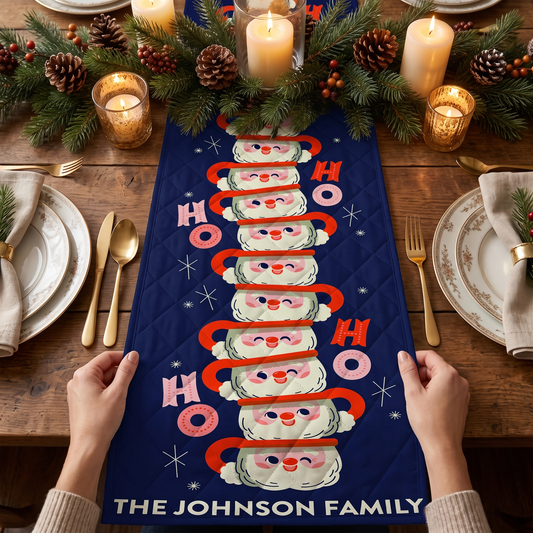 Hands holding a navy quilt table runner with a tall stack of Santa face mugs, pink HO HO HO letters and custom family name