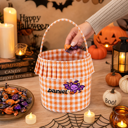 Hand dropping candy into an orange gingham ruffle bucket with purple bat embroidery and custom name
