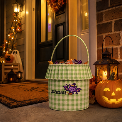 Green gingham ruffle Halloween bucket with purple witch hat bat and custom name next to a jack o lantern at a door