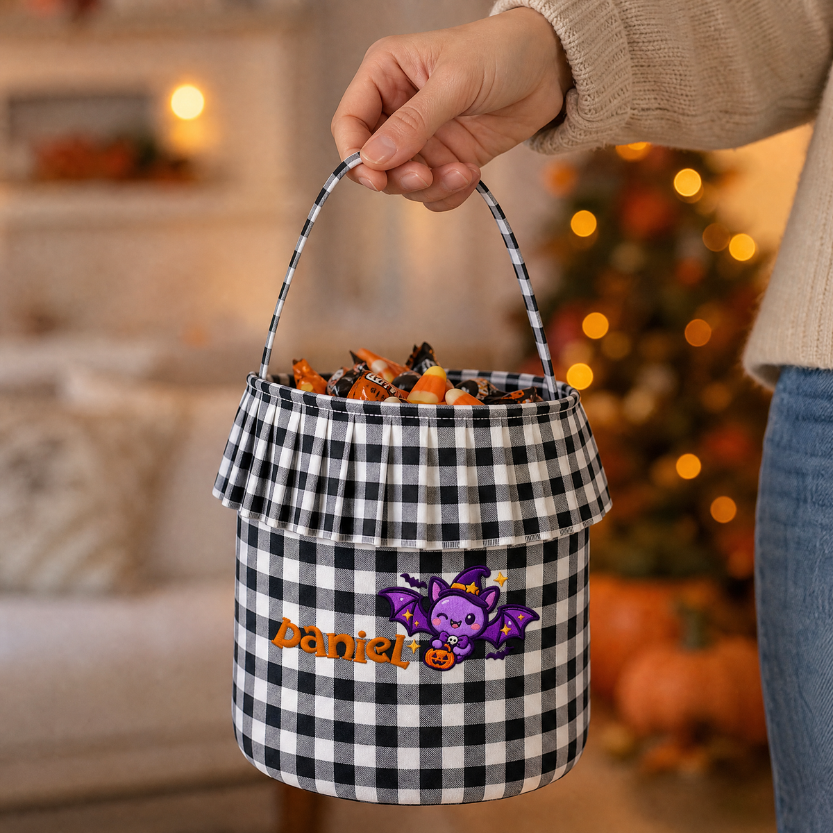Hand carrying a black and white gingham ruffle candy bucket with purple bat and orange custom name embroidery