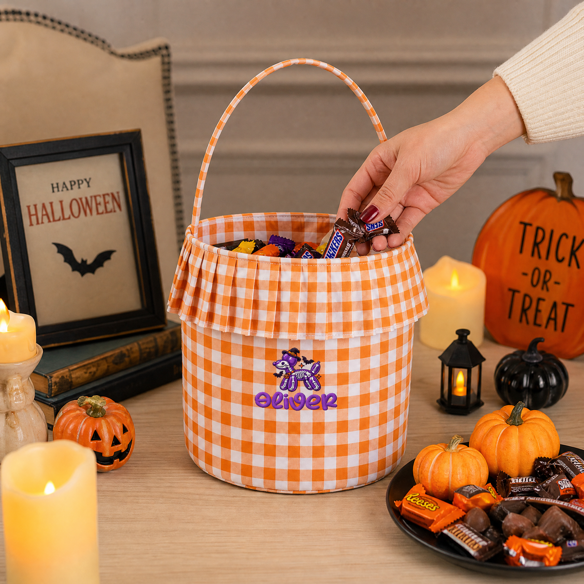 Hand adding candy to an orange gingham ruffle bucket embroidered with a purple balloon dog and custom name
