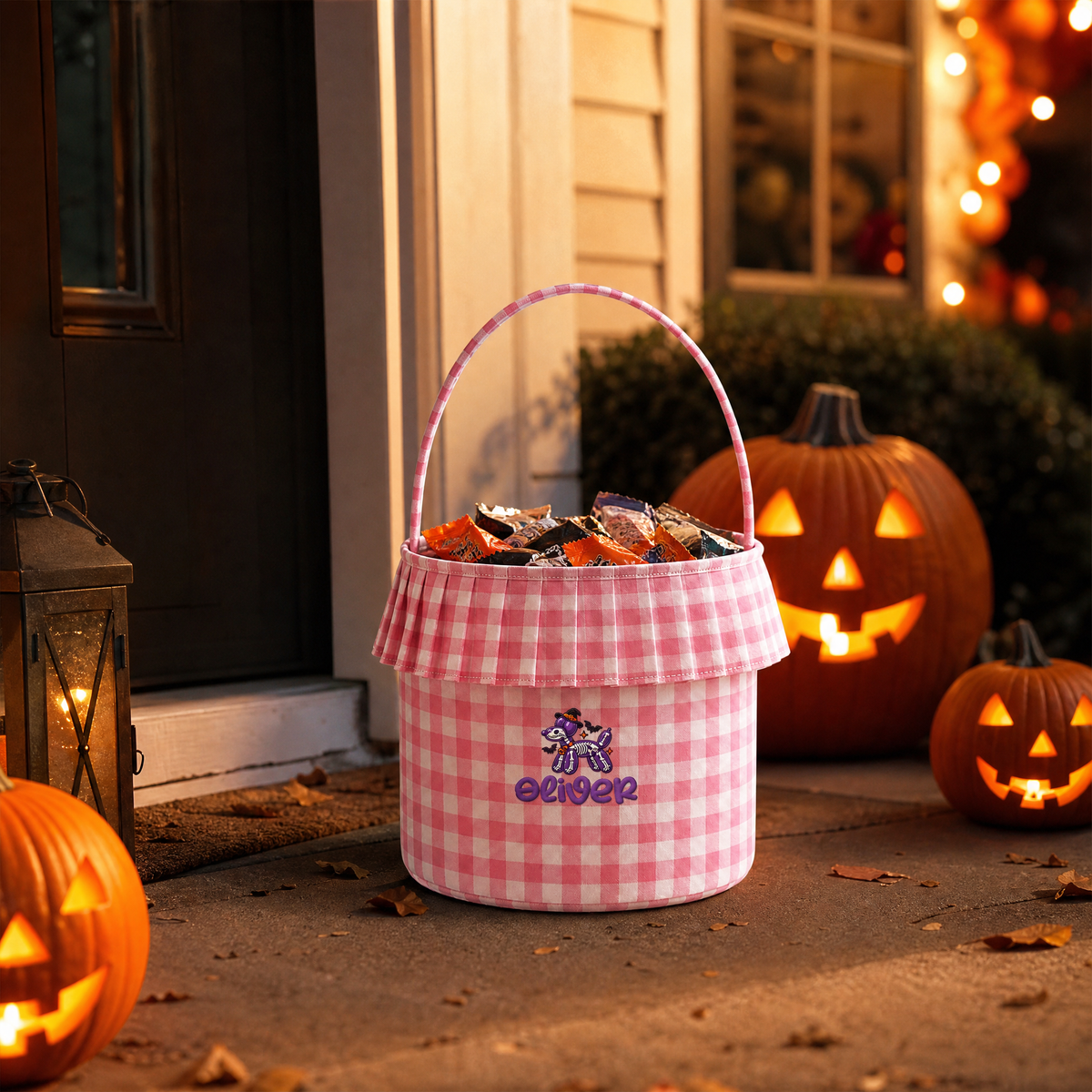 Pink gingham ruffle trick or treat basket with skeleton balloon dog embroidery filled with candy on a porch