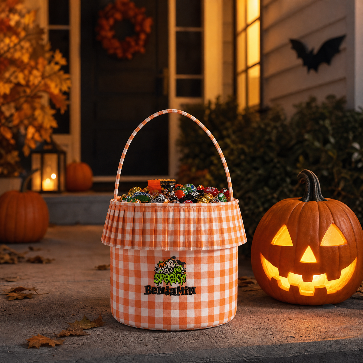Orange gingham ruffle bucket full of candy with Let's Get Spooky embroidery beside a glowing jack o lantern on a porch