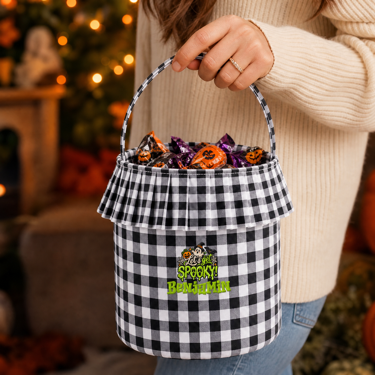 Woman holding a black and white gingham ruffle candy basket with green Let's Get Spooky custom name embroidery