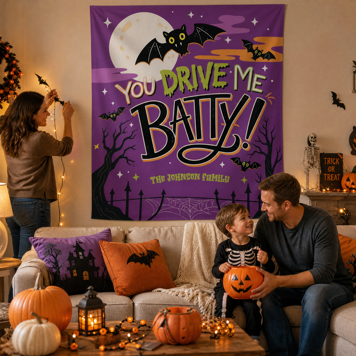 Family decorating for Halloween under a personalized You Drive Me Batty tapestry with a child in a skeleton costume