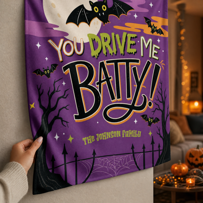 Close up of hand holding the corner of a purple bat tapestry printed with You Drive Me Batty and a custom family name