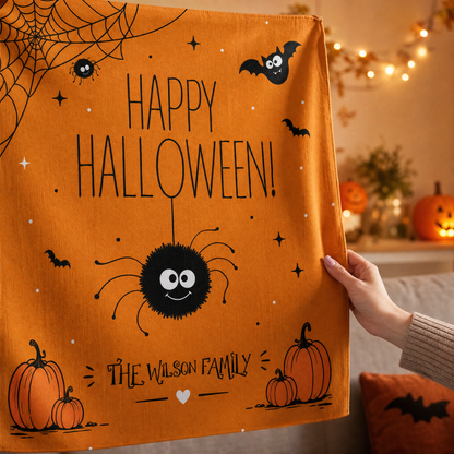 Hand lifting the corner of the orange Happy Halloween spider tapestry with a custom family name